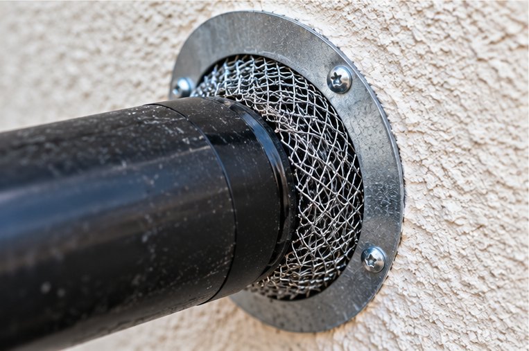 A stainless mesh collar sealed around a soil pipe where it passes through a rendered wall
